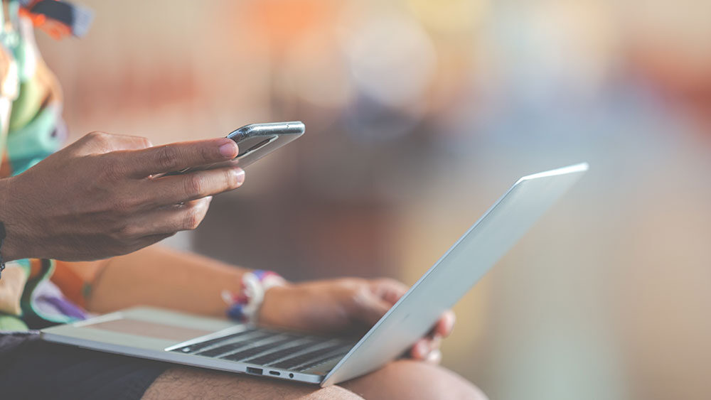 Seorang laki-laki sedang memegang handphone dan laptop